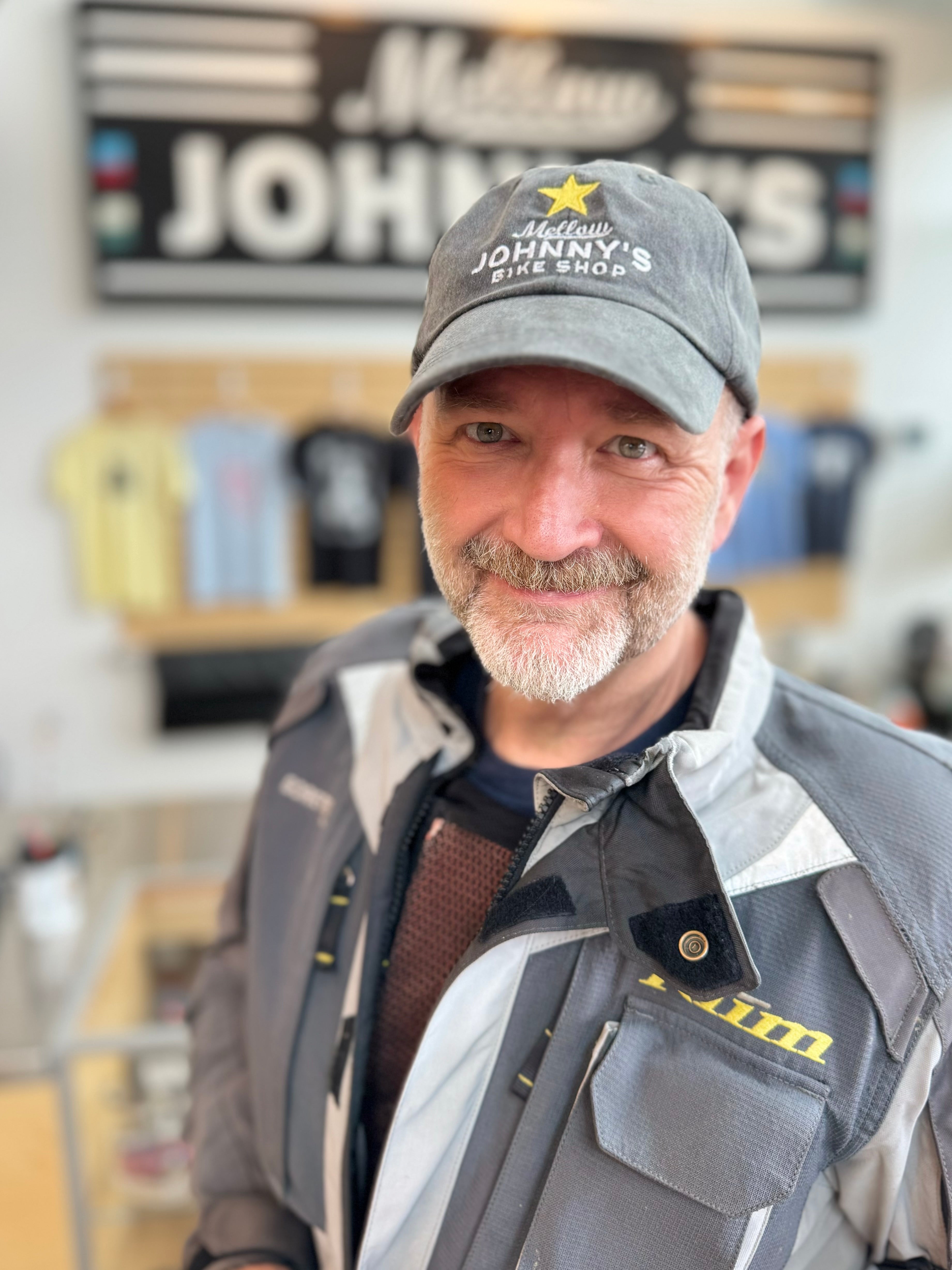 A person wearing a gray baseball cap with a Mellow Johnny's logo on it, standing in front of a store counter.